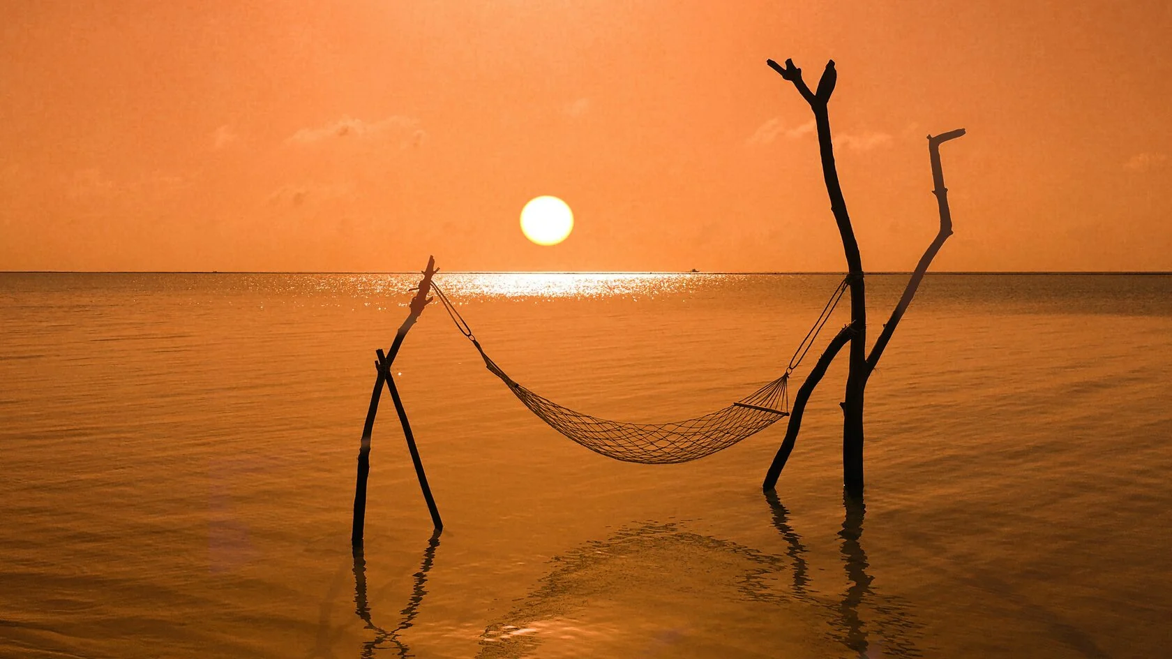 A hammock suspended above the sea at a golden Maldivian sunset